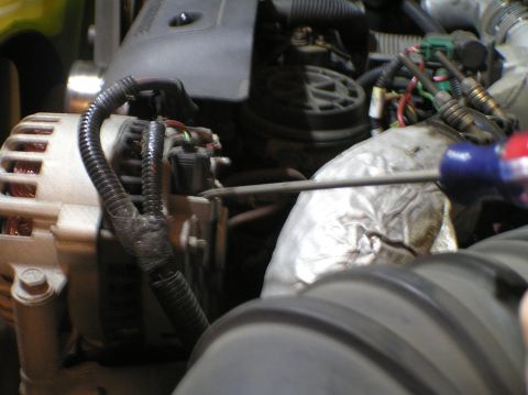 2000 Ford Excursion - Close-up view of an alternator and surrounding engine components, with a screwdriver engaged.