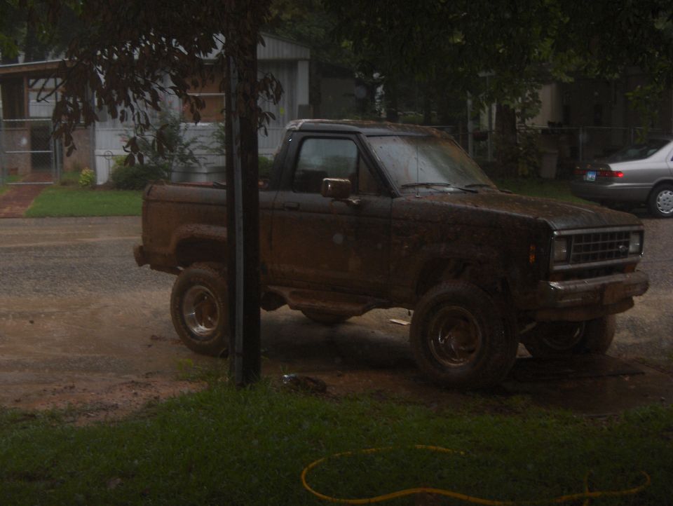 Mud-covered dark brown Ford Ranger pickup truck parked on a wet, muddy road