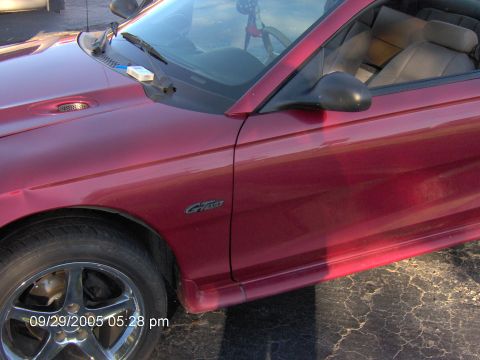 1996 Ford Mustang - A red 1996 Ford Mustang GT convertible is shown from the front quarter angle.