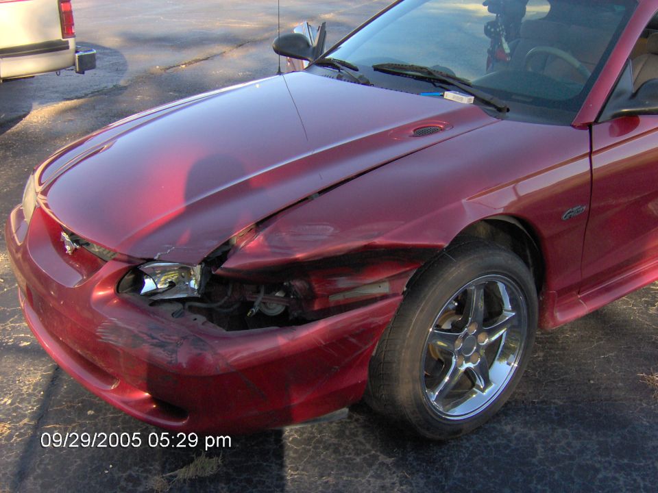 Red car with front-end damage, parked next to a pickup truck. Timestamp 09/29/2005