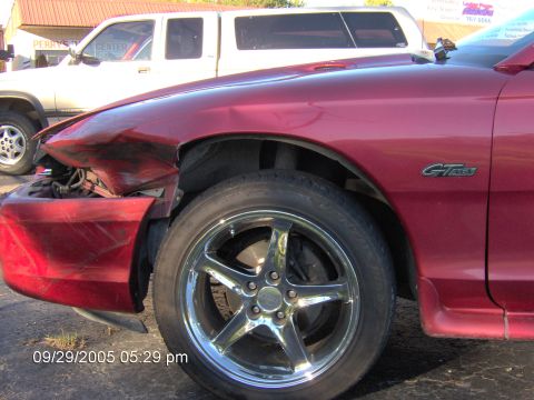 1996 Ford Mustang - Front fender of a red car is heavily damaged, revealing the GT badge and a chrome five-spoke wheel.