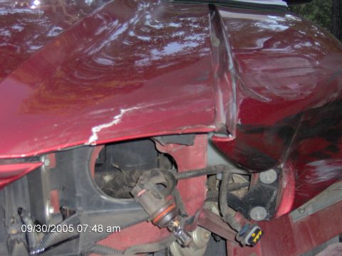 1996 Ford Mustang - The front fender of a red car shows damage and exposed components, including wiring and a light socket.