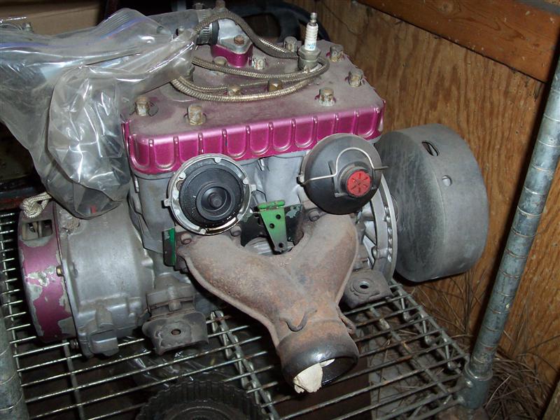 Small engine with pink-painted cylinder and exhaust manifold sitting on wire shelving