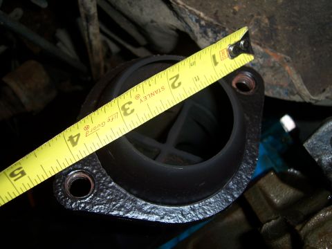 1983 Ford Bronco - A close-up view of a vehicle part, likely a thermostat housing, being measured with a tape measure.