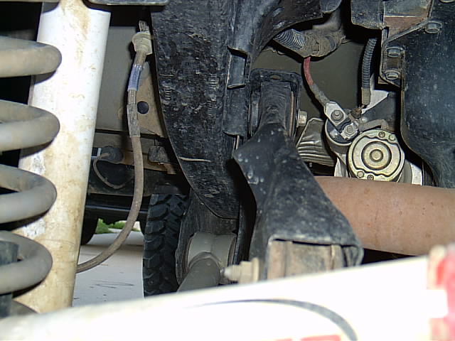 Lifted truck underbody showing coil spring, bracket, brake line and tire