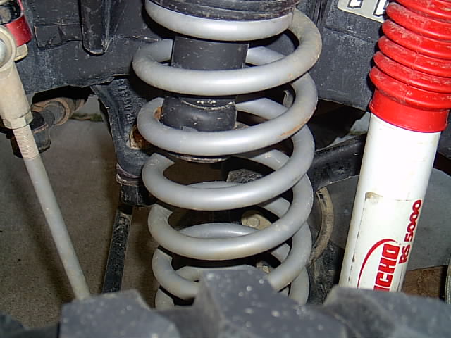 Gray coil spring beside a red and white Rancho RS5000 shock under a vehicle