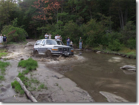 1995 Ford Bronco - A Ford Bronco navigates a challenging off-road water crossing with onlookers present.