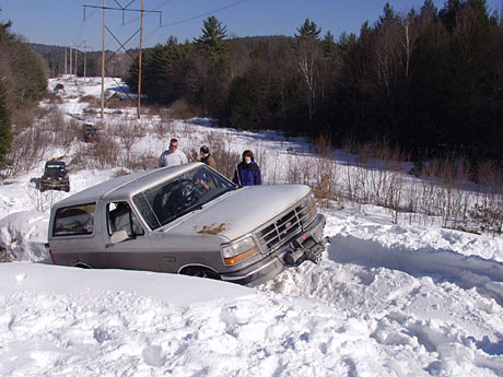 1995 Ford Bronco - A 1995 Ford Bronco is stuck in deep snow on a winter day, with other vehicles in the distance.
