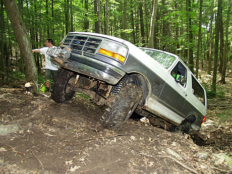 1995 Ford Bronco - A 1995 Ford Bronco navigates a challenging, muddy off-road course in a wooded area.