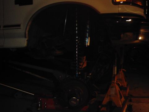 1978 Ford Bronco - The rear suspension of a white vehicle is visible, supported by jack stands and showing blue shocks.