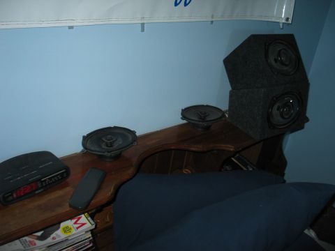 1995 Ford Bronco - Several car speakers are arranged on a wooden surface, accompanied by a clock radio and a remote control.
