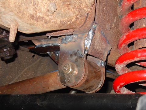 1995 Ford Bronco - Close-up of a welded suspension bracket and a red coil spring, likely from a vehicle's undercarriage.