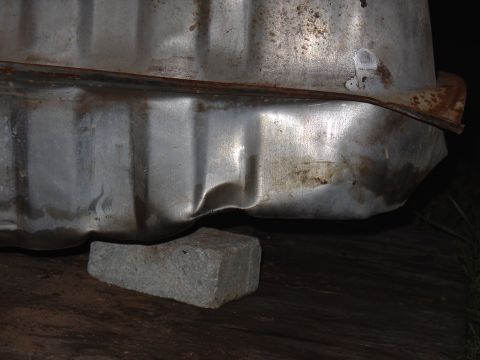 1995 Ford Bronco - A close-up view shows a dented metal tank resting on a brick.