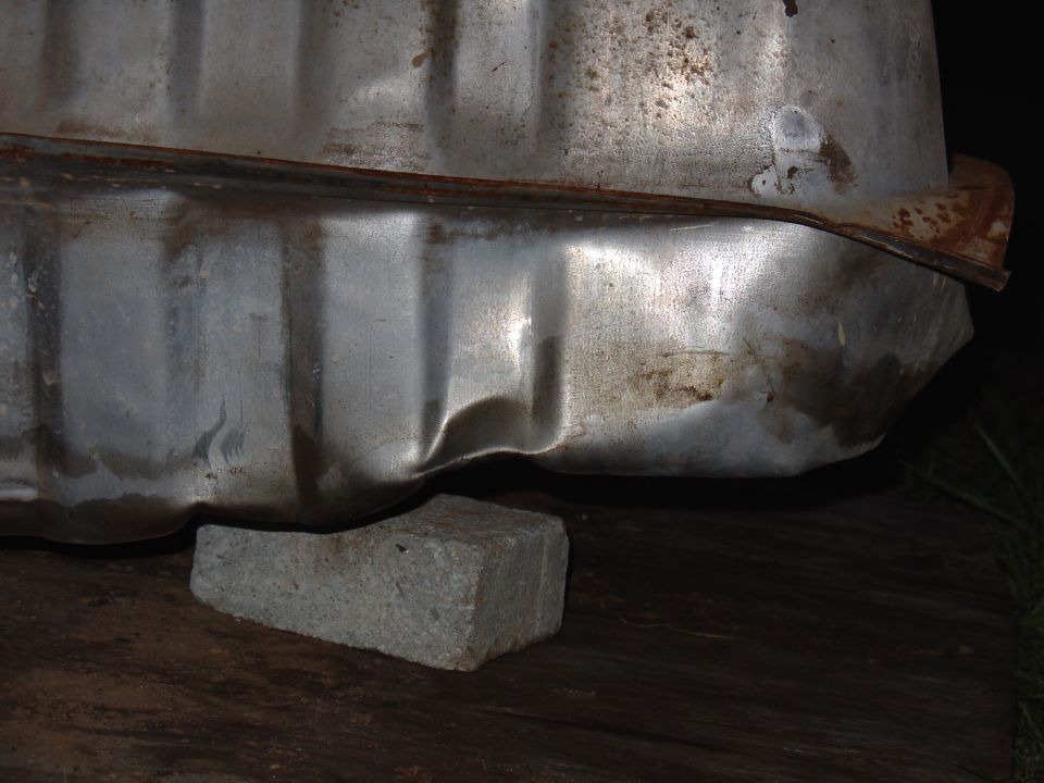 close-up of a dented metal tank supported by a brick