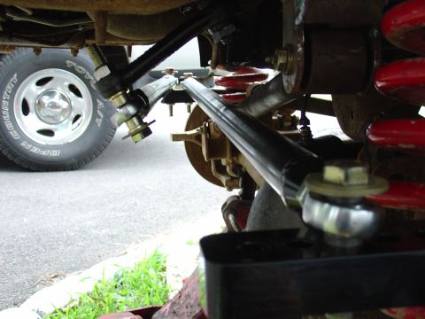 1995 Ford Bronco - The image shows the suspension system of a vehicle, including red coil springs and black control arms, with a tire in the background.