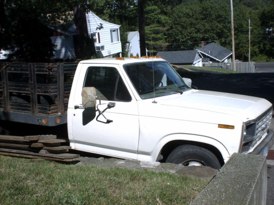 White pickup truck with a wooden flatbed stuck in a ditch next to a concrete barrier