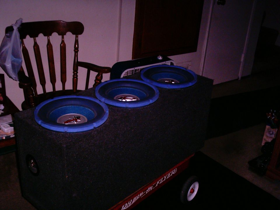 Subwoofer box with three blue-rimmed speakers sits on a red Radio Flyer wagon