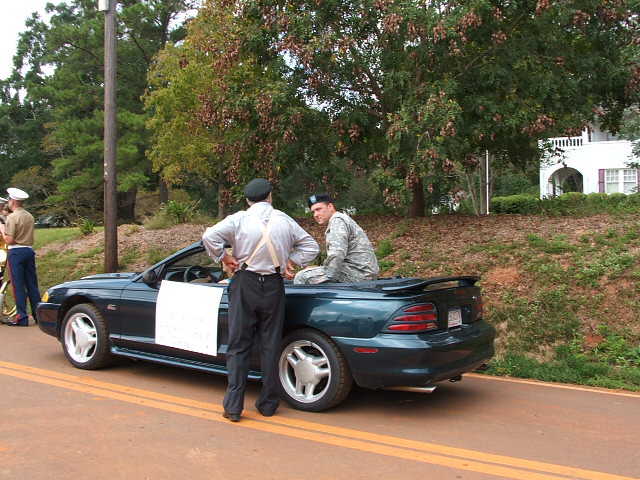 Dark green convertible with a spoiler, seen from the rear-right quarter. It has aftermarket wheels and white panels on the doors