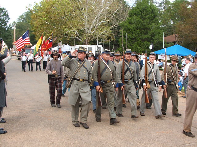 Civil War reenactors marching in a parade, carrying rifles and flags