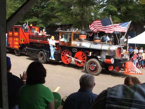 1966 Ford Ranchero - A unique parade vehicle combines a steam locomotive front with a fire truck trailer, drawing attention from onlookers.