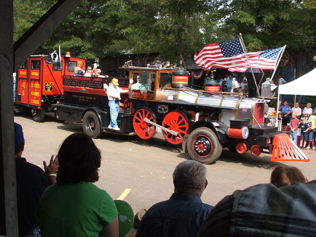 Custom locomotive vehicle with a fire truck trailer, decorated with American flags, in a parade