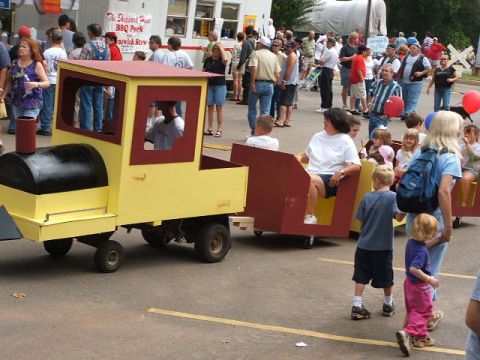 1966 Ford Ranchero - A toy train with passenger cars carries people through a crowd at an outdoor event.