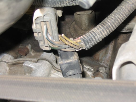 Gray wiring harness connector with colored wires in a dusty engine bay