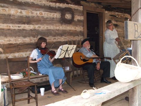 1966 Ford Ranchero - A woman plays the violin while a man plays the guitar on a porch, with another woman standing nearby.