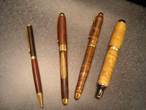 1995 Ford Bronco - A collection of four pens, each with a unique wooden barrel and gold trim, are displayed on a dark, textured surface.