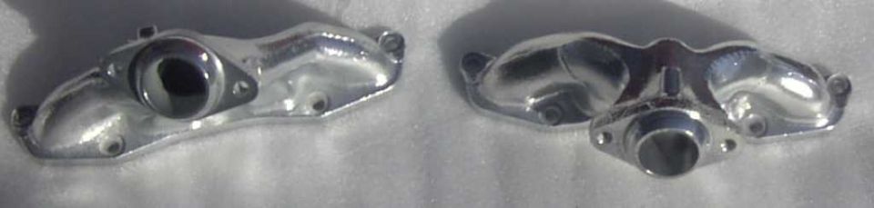 Two chrome exhaust manifold parts on a white surface