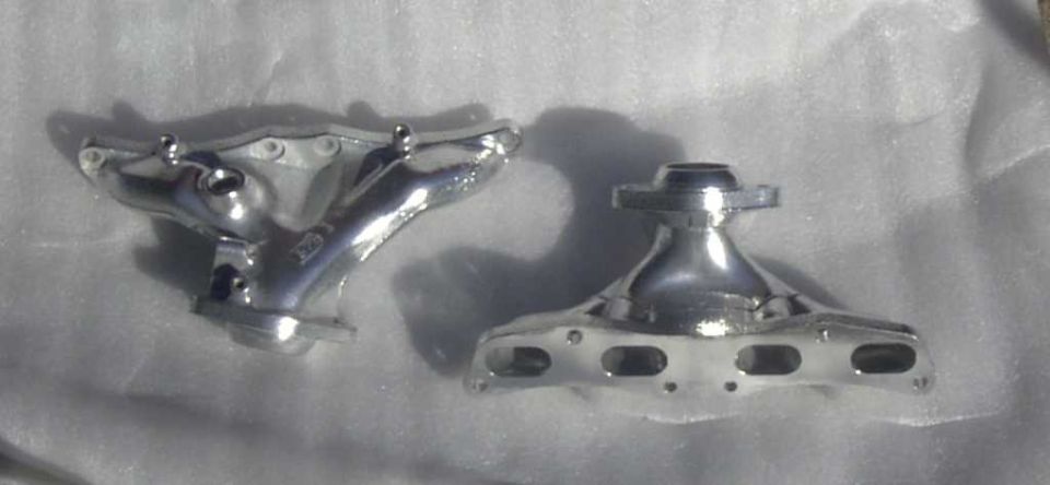 Two chrome exhaust manifolds on a white surface. One is a Y-pipe style, the other is a more compact design