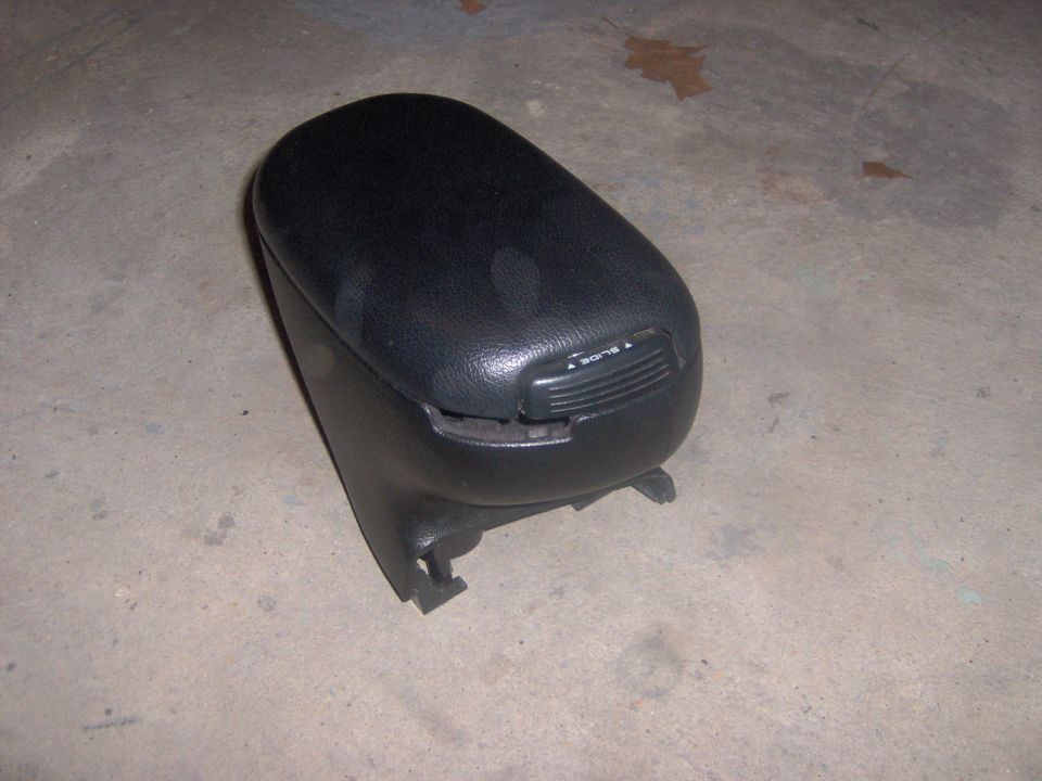 Black automotive center console armrest lid removed and placed on concrete floor