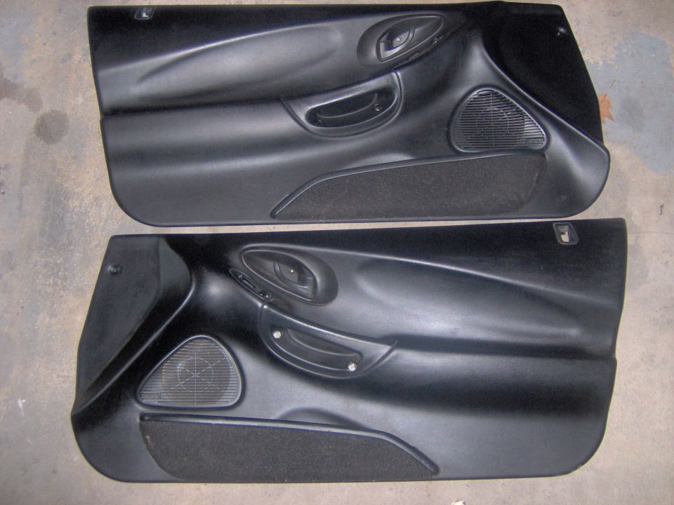 Pair of black coupe door panels with speakers laid on a concrete floor