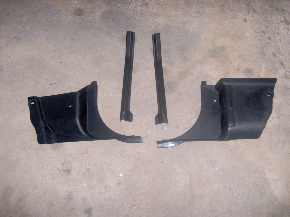 Two black plastic door sill trim pieces and two black plastic A-pillar trim pieces laid out on a concrete floor