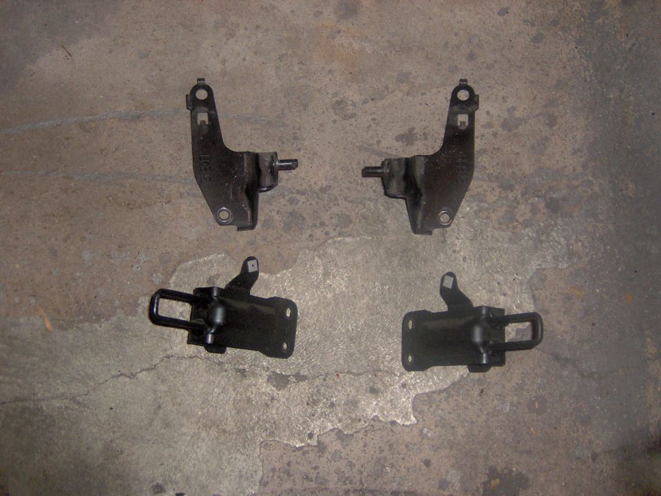 Four black car door hinges laid out on a concrete surface