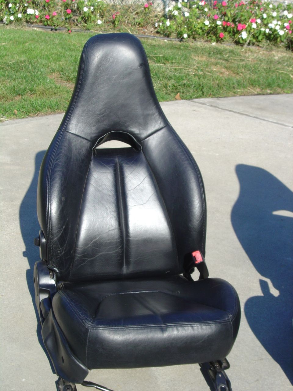 Black leather car seat with red seatbelt buckle, sitting on concrete