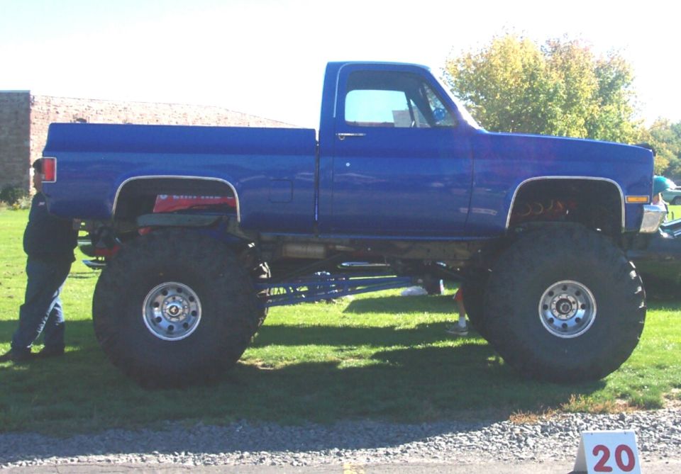 Blue lifted pickup truck with massive tires, side view. Chrome wheels visible