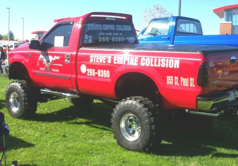 1979 Ford F-150 - A red pickup truck with custom modifications and company branding is parked on a grassy field next to a blue truck.