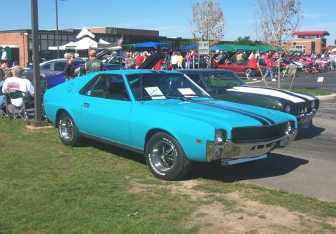 1979 Ford F-150 - A bright blue 1970 AMC Javelin, distinguished by its racing stripes, is showcased at an outdoor event alongside other vehicles.
