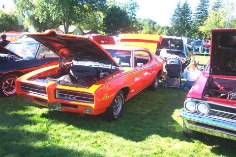 1979 Ford F-150 - Orange 1969 Pontiac GTO at a car show, hood open, with other vehicles nearby.