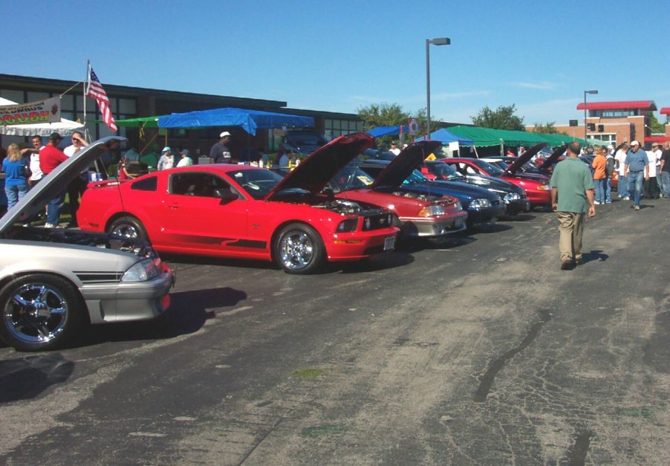 Red Ford Mustang with hood open, parked in a line of cars