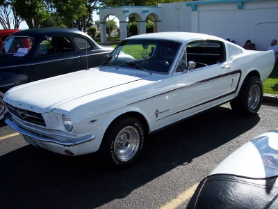 1972 Ford Ranchero - A white 1965 Ford Mustang fastback is seen from a three-quarter front angle, parked next to another vehicle.