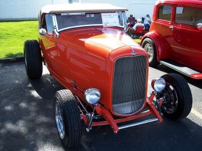 1972 Ford Ranchero - An orange hot rod is parked next to a red sedan at an outdoor event.