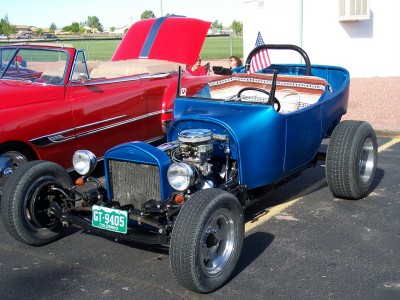 1972 Ford Ranchero - A blue hot rod roadster is parked next to a red convertible with its hood up.