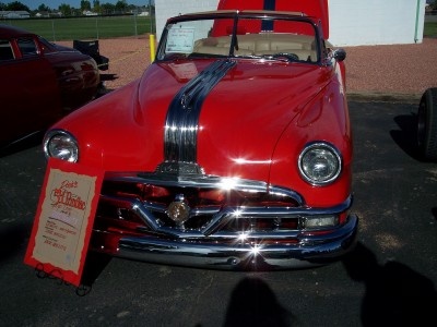 1972 Ford Ranchero - A red convertible with a prominent chrome grille and hood stripe is displayed at an event.