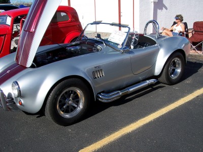 1972 Ford Ranchero - A silver Shelby Cobra is displayed with its hood open, parked beside a red classic car at an outdoor event.