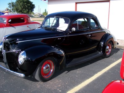 1972 Ford Ranchero - A black 1940 Ford coupe is parked next to another vehicle. The car has red wheels.