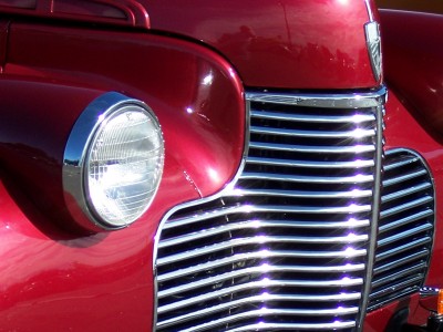 1972 Ford Ranchero - Close-up view of the shiny chrome grille and round headlight on a vintage red automobile.
