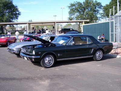 1972 Ford Ranchero - A dark green 1965 Ford Mustang coupe is parked with its hood open, alongside other vehicles.