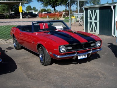 1972 Ford Ranchero - A red convertible with black racing stripes is parked outdoors near a green shed and a fence.